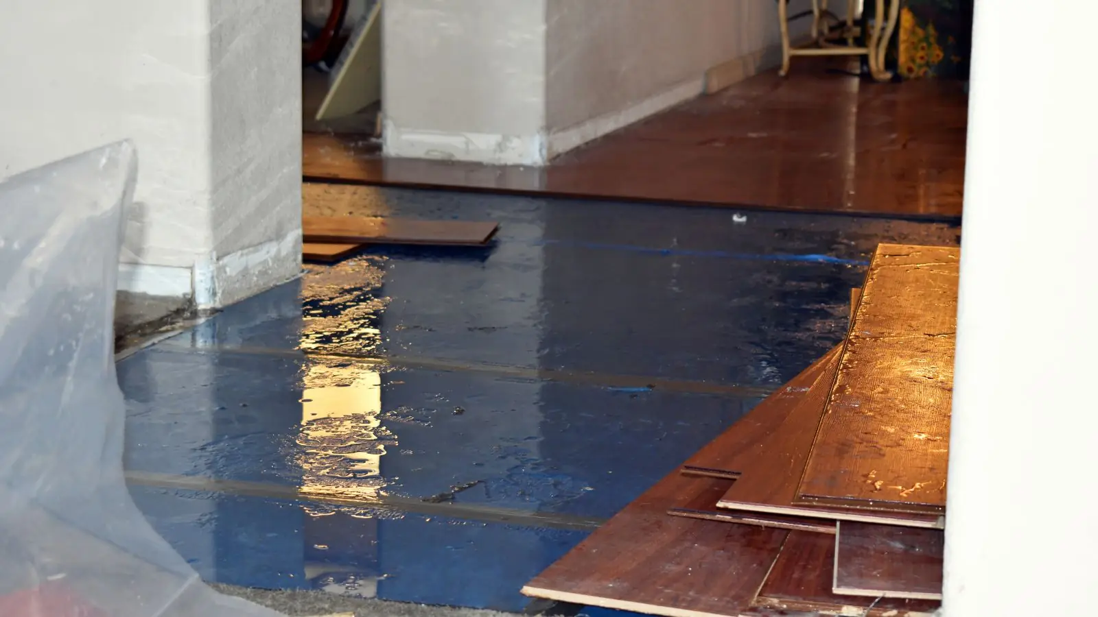 Hardwood boards pulled up over a wet blue underlayment during floor water damage repair